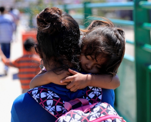 A young migrant child carried by her caretaker