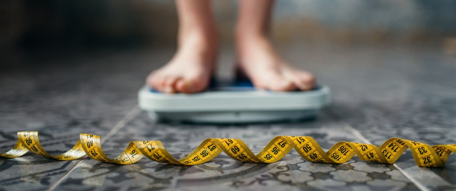 A woman's feet standing on a bathroom scale with a tape measure on the floor