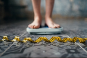 A woman's feet standing on a bathroom scale with a tape measure on the floor