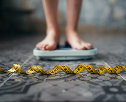 A woman's feet standing on a bathroom scale with a tape measure on the floor