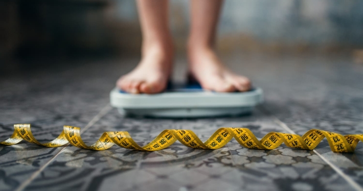 A woman's feet standing on a bathroom scale with a tape measure on the floor