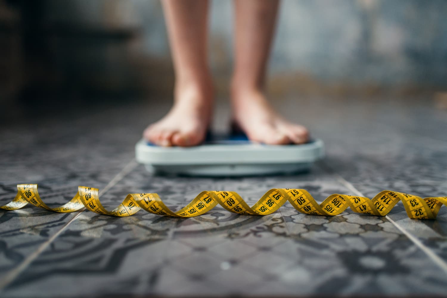 A woman's feet standing on a bathroom scale with a tape measure on the floor