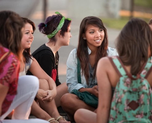 A group of teen girls sit talking with each other in a supportive manner