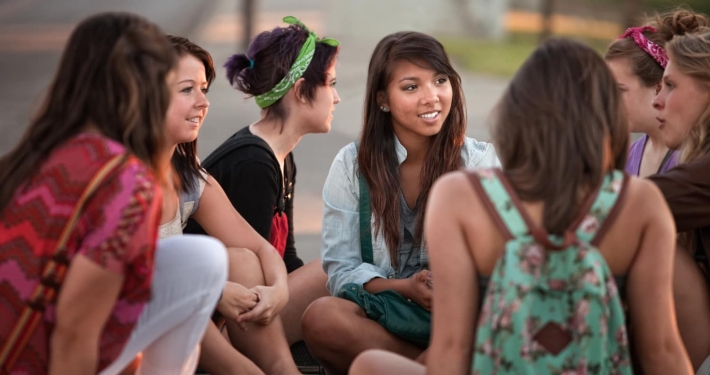 A group of teen girls sit talking with each other in a supportive manner