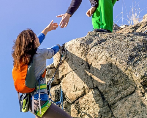 Two climbers reaching summit, one holding hand of her partner assisting to make last step to top