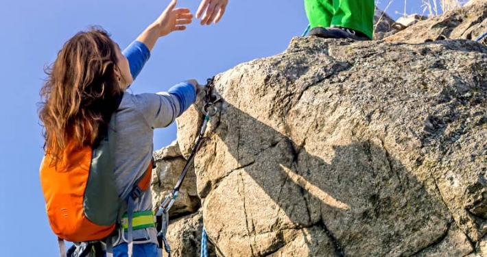 Two climbers reaching summit, one holding hand of her partner assisting to make last step to top