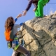 Two climbers reaching summit, one holding hand of her partner assisting to make last step to top